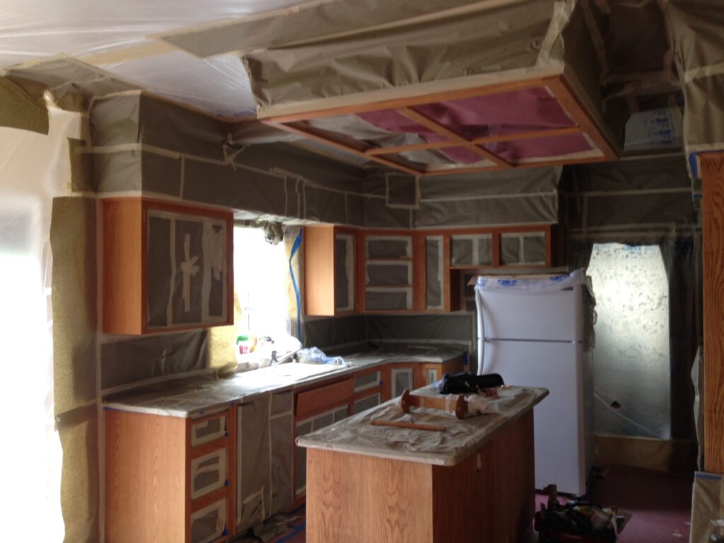 Kitchen under renovation with covered cabinets, island, and appliances wrapped in protective materials.