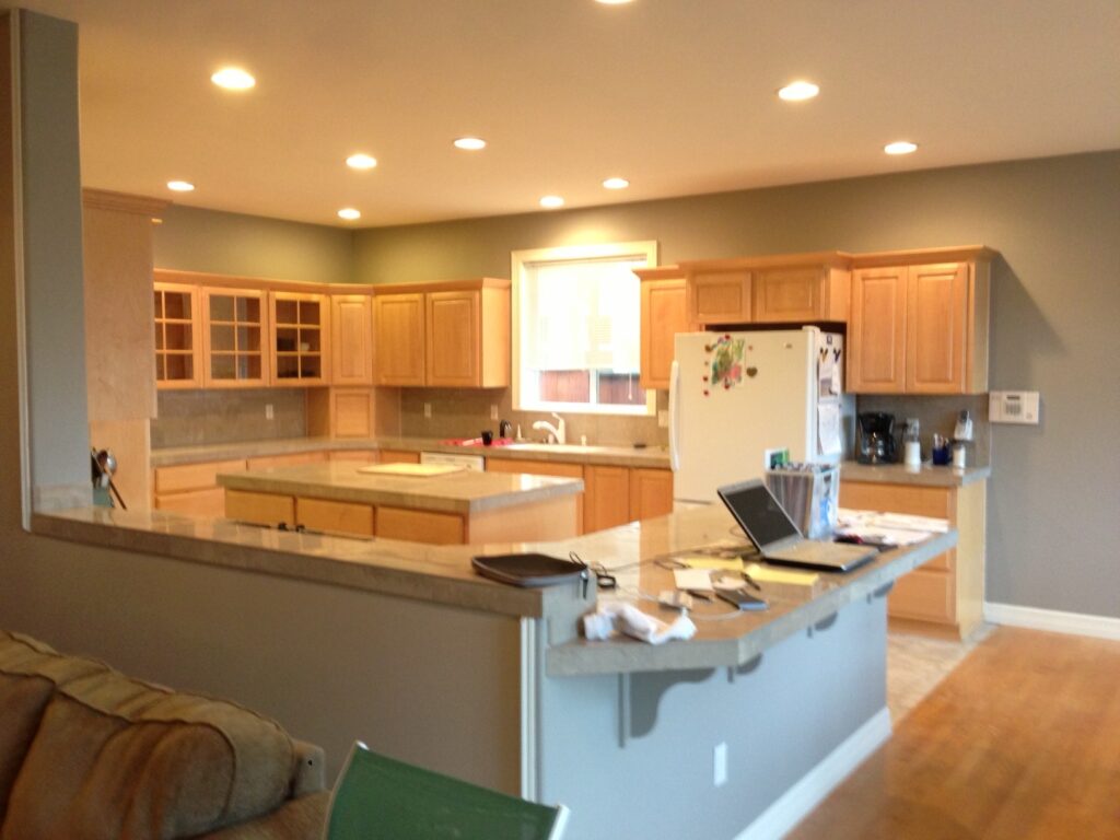 Modern kitchen with wooden cabinets, recessed lighting, and a central island. Laptop and papers on the counter.