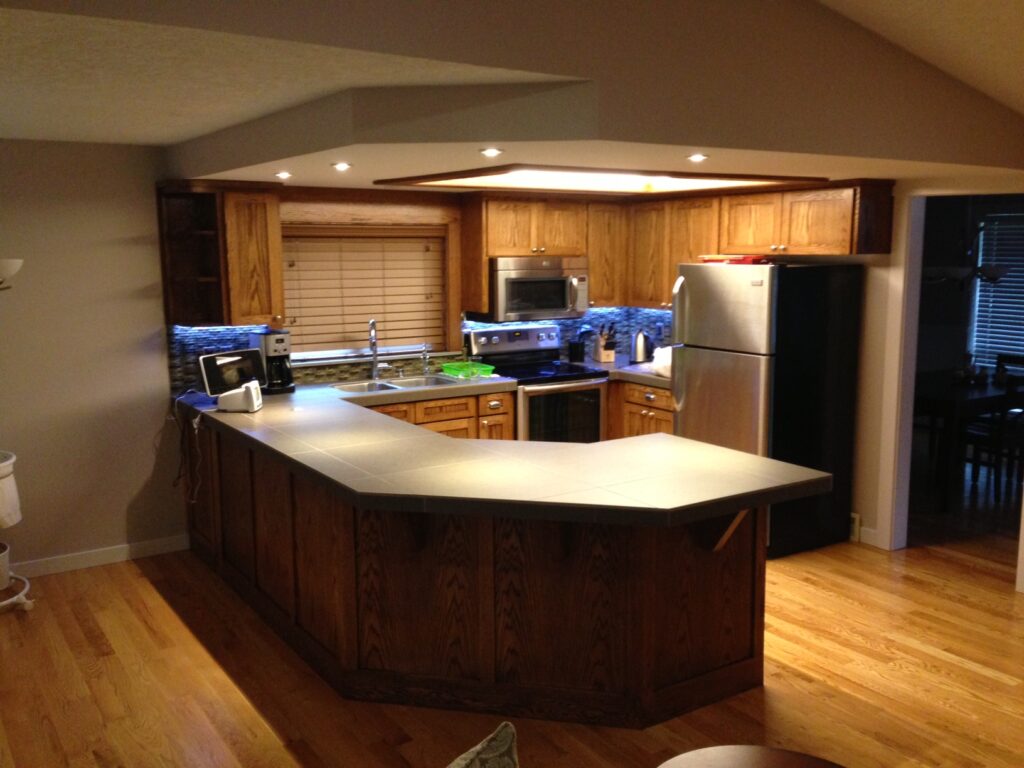 Home kitchen with wooden cabinets, stainless steel appliances, and under-cabinet lighting. Features a gray tile countertop.