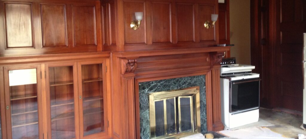 Room with wood-paneled walls, built-in cabinets, a fireplace with a green marble surround, and a white oven next to it.