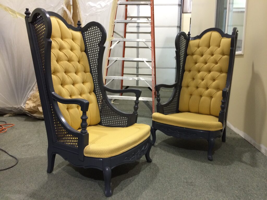 Two high-back chairs with dark wooden frames and yellow tufted cushions are set in a room with a ladder in the background.