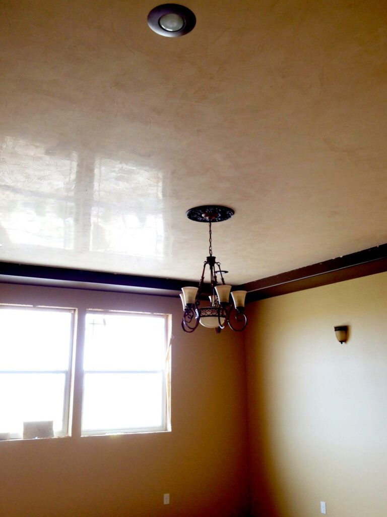 Room with beige walls, a reflective ceiling, a central light fixture, two windows, and one wall lamp.